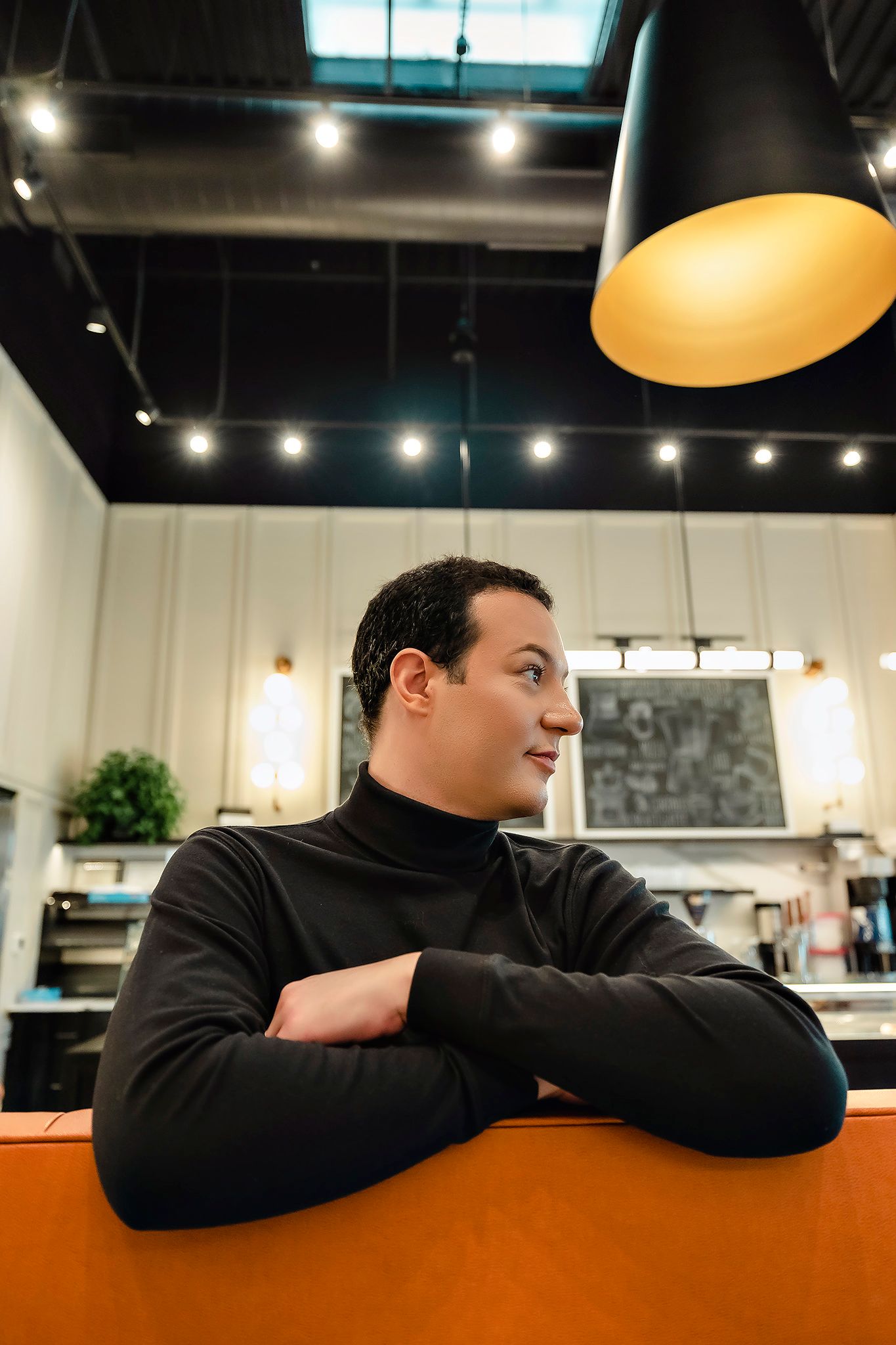 Person in black sweater leans on orange counter in modern cafe setting.