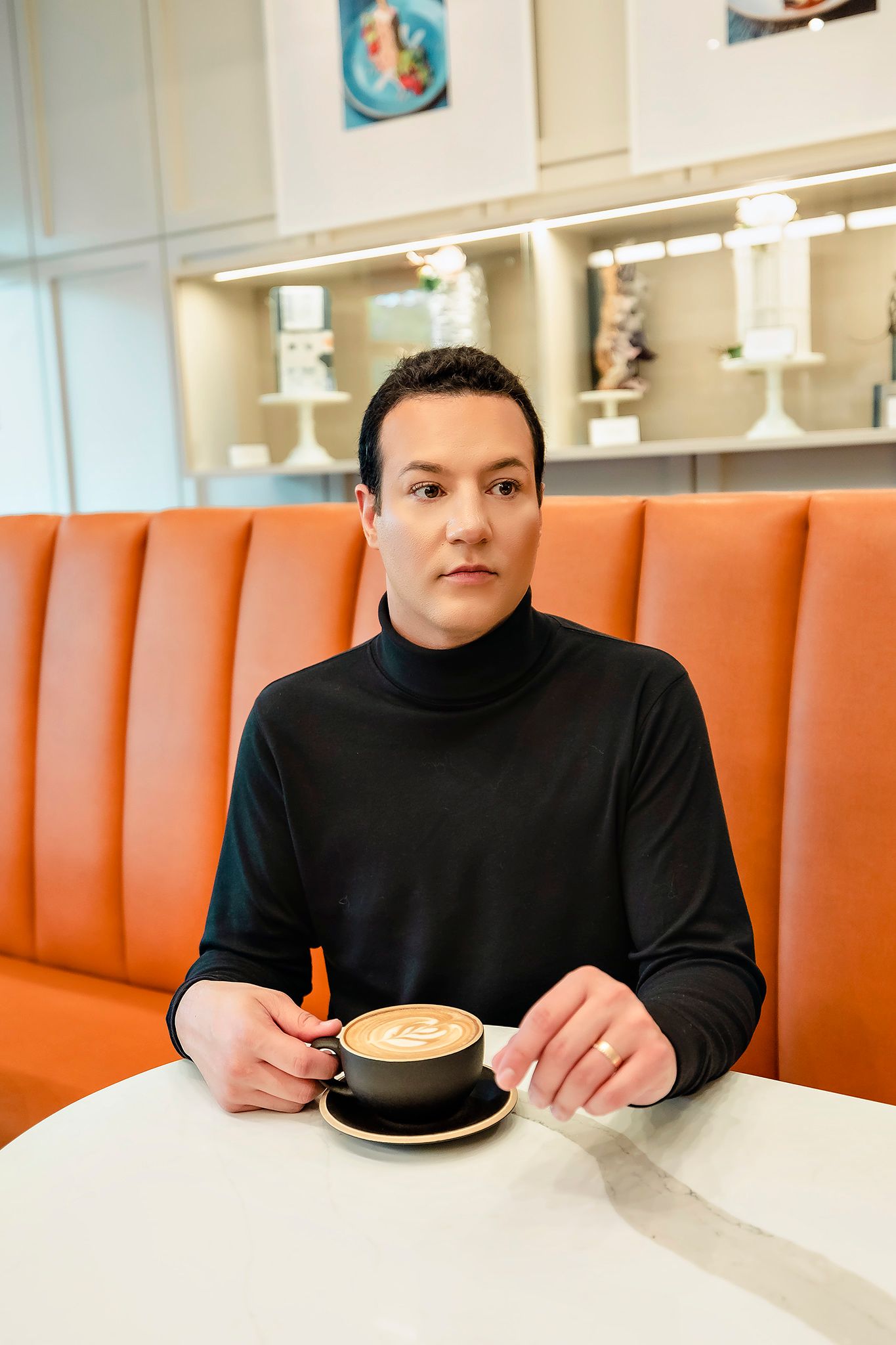 Person in black sweater sitting at diner booth with orange seating and white marble table with coffee.