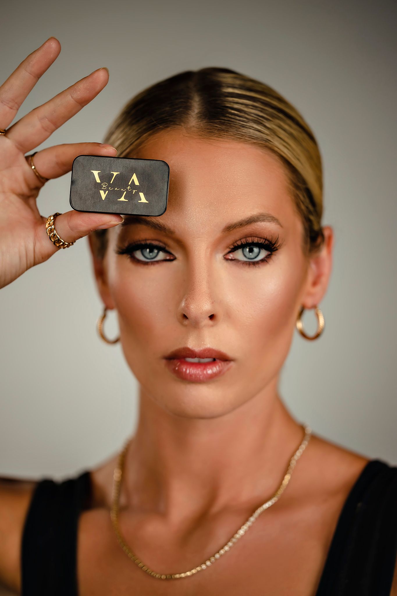 Model demonstrating makeup product in close-up beauty photography against gray background.