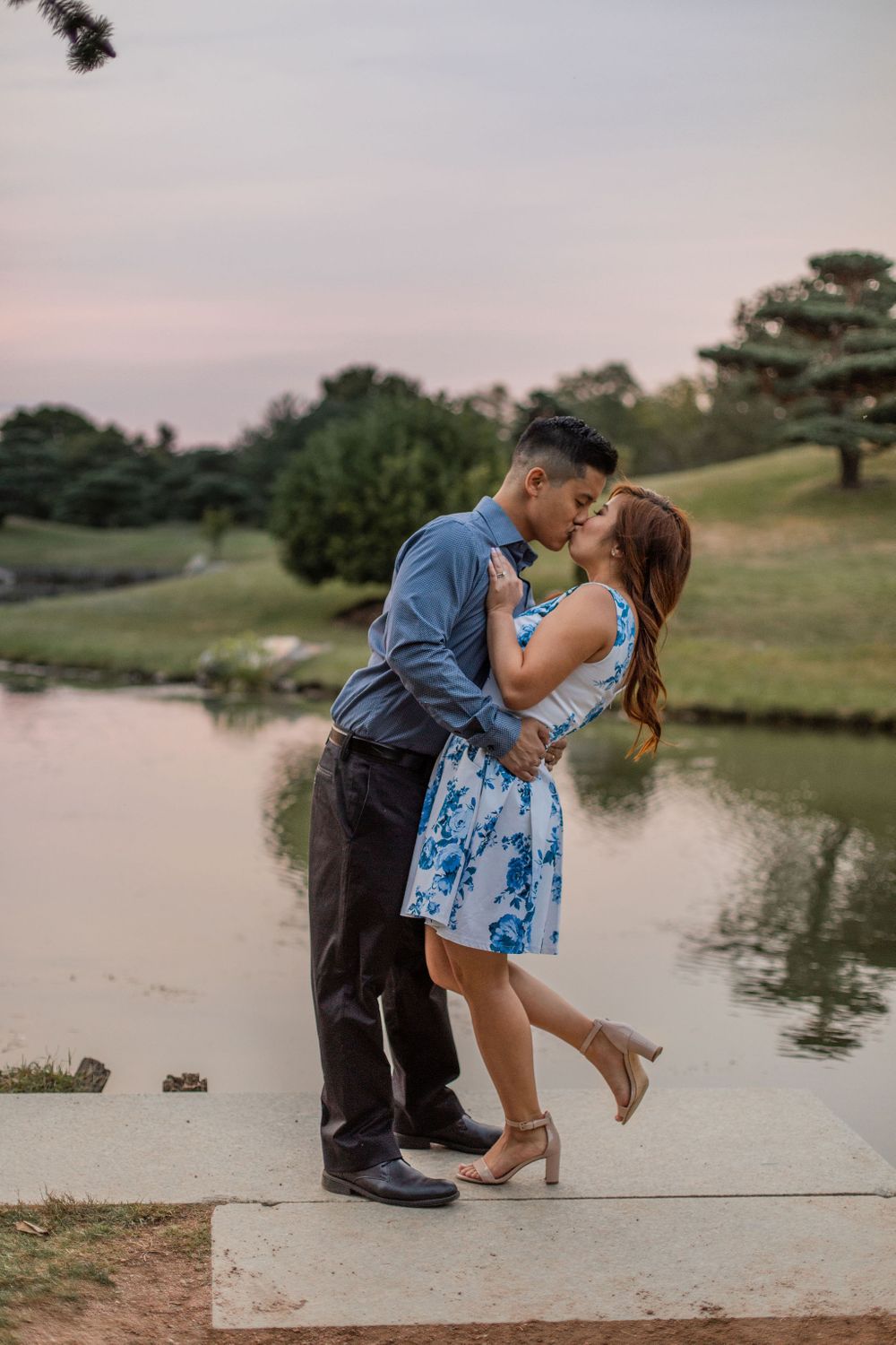 A romantic couple shares a kiss by the lake during sunset.