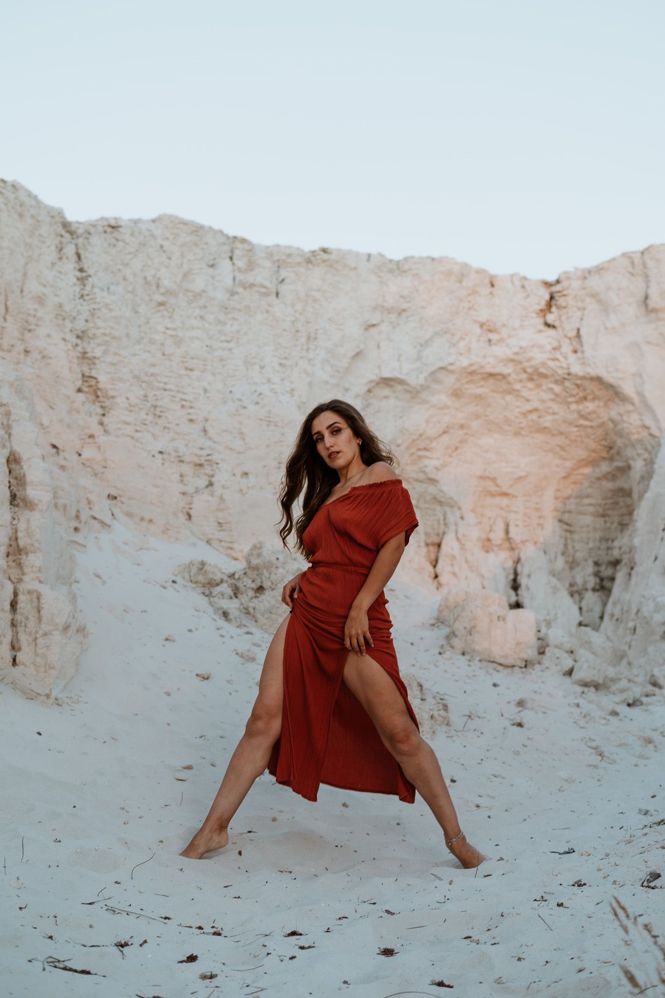 Woman in flowing red dress poses dramatically against white limestone cliffs.