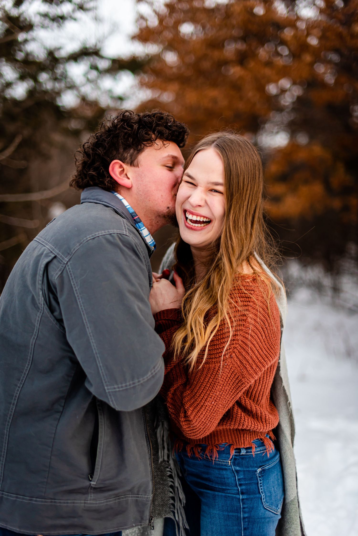 A joyful winter moment captured between a couple against autumn foliage.