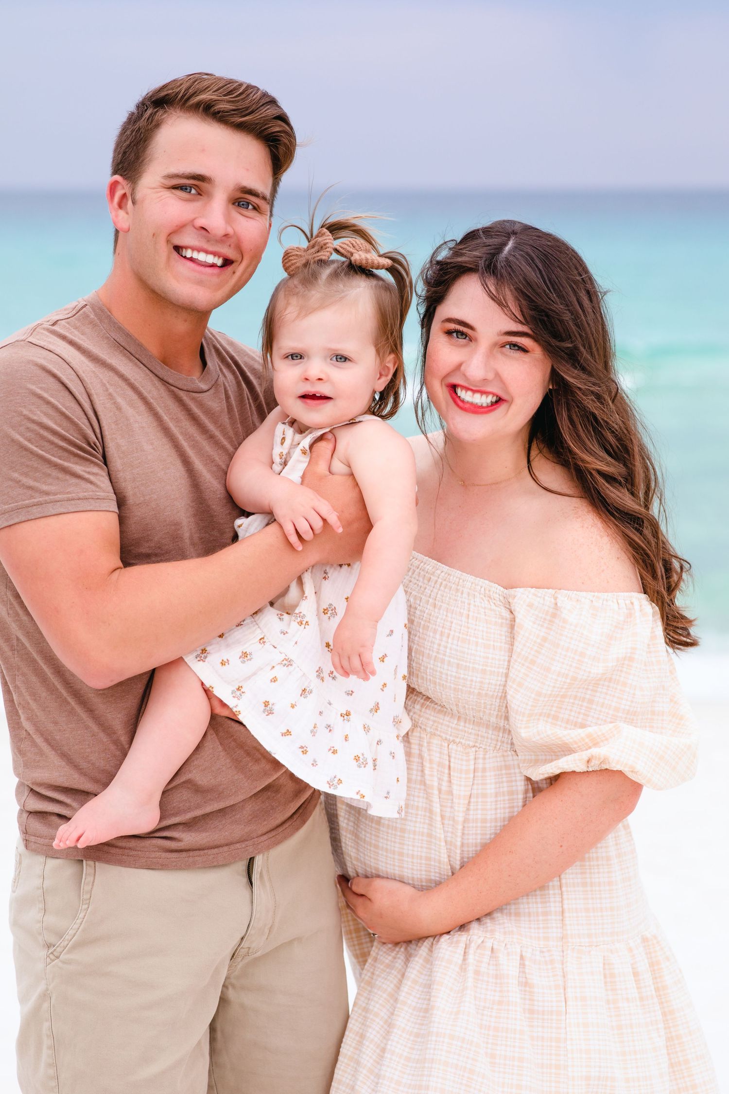A family poses together in casual attire against a stunning turquoise ocean backdrop on a sunny day.
