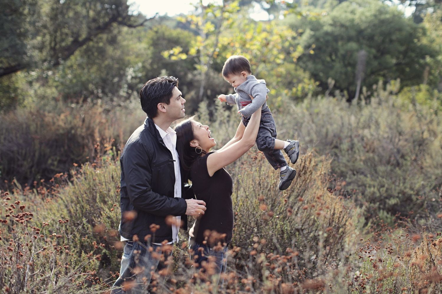 Family playing together in tall grass during golden hour.