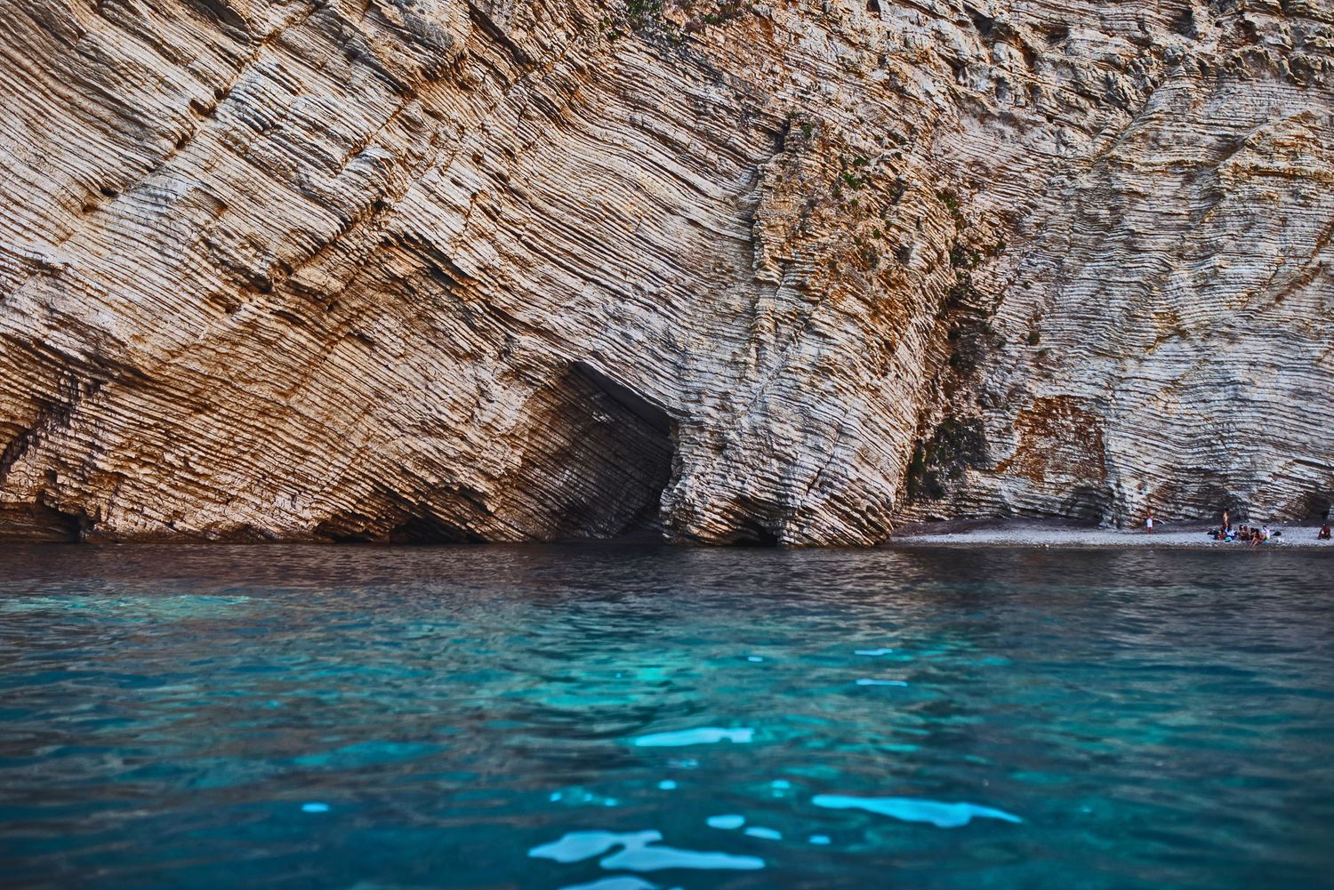 Rugged limestone cliff face meeting turquoise Mediterranean waters with stunning geological formations.