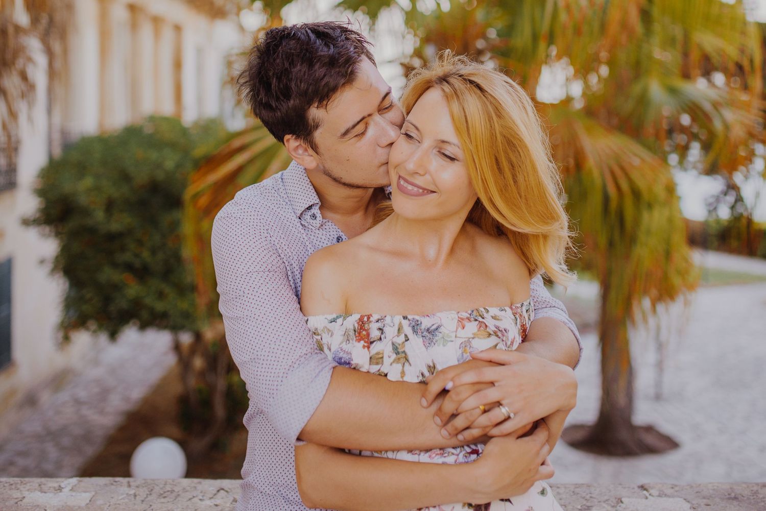 Intimate moment captured in a tropical garden setting with palm trees and warm lighting.