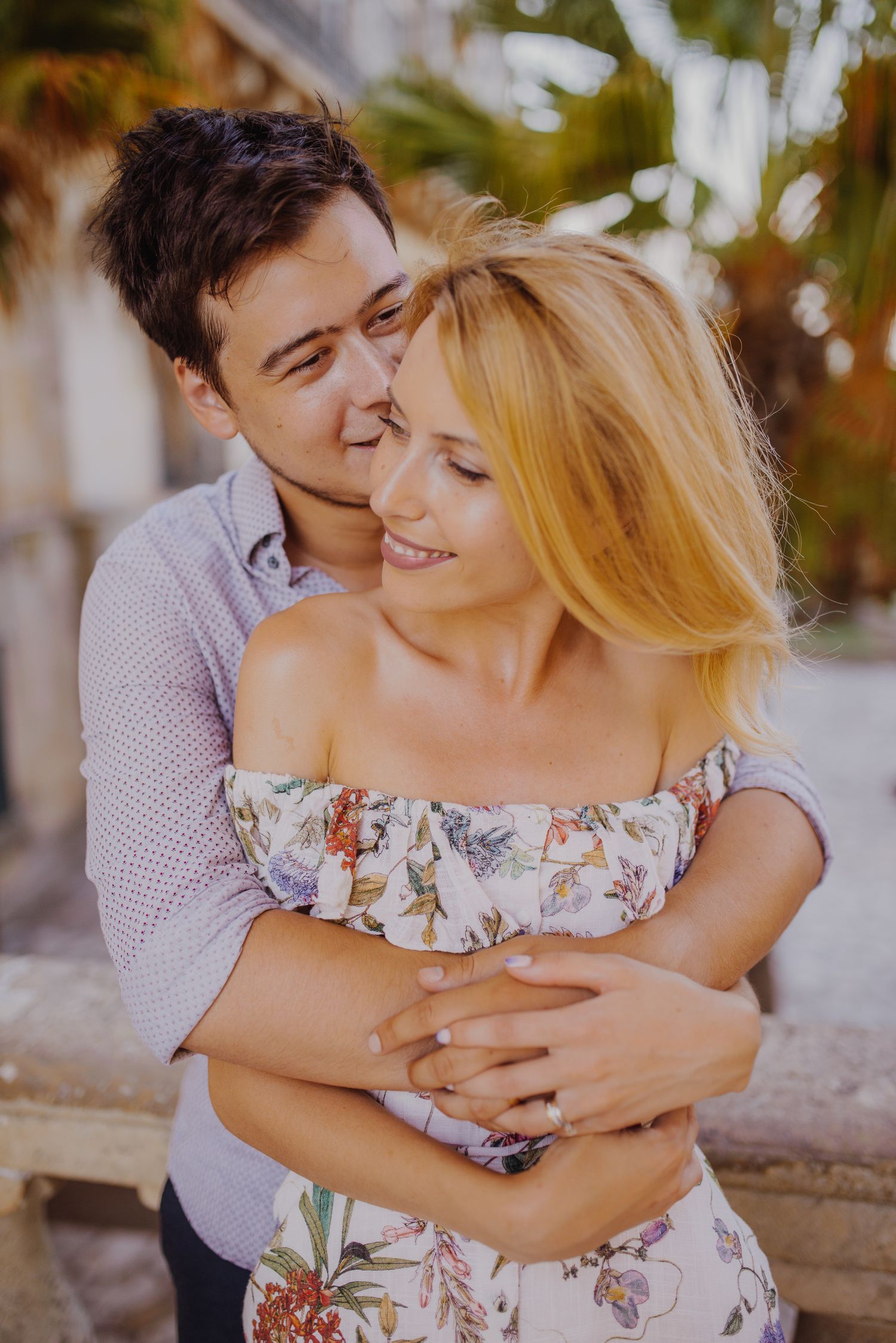 Romantic couple embracing in a floral dress and casual shirt against a stone backdrop.