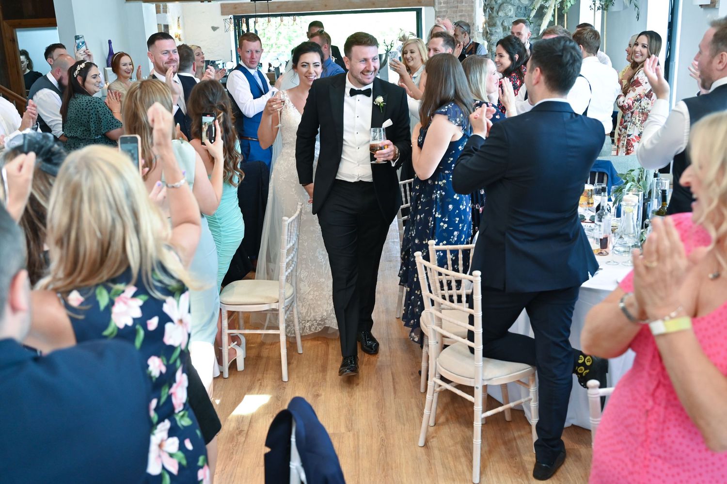 Wedding guests applaud during a reception celebration in an elegant venue.