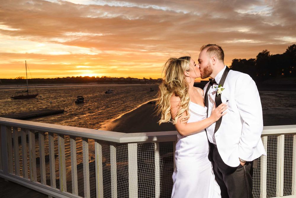The bride and groom share a kiss posing for a portrait during sunset on their wedding day.