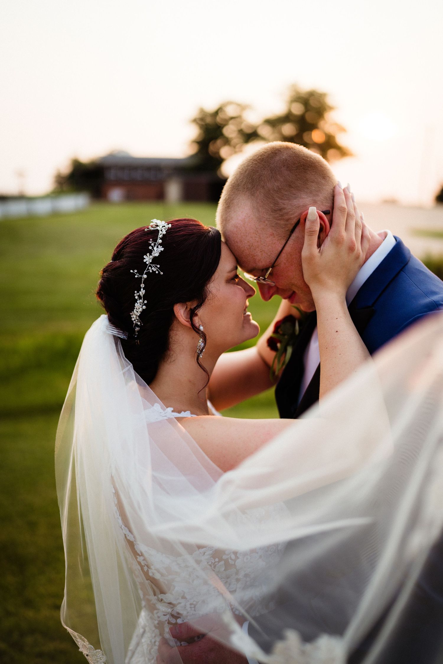 A tender moment between newlyweds as the bride's veil flows in the golden evening light.