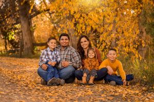 Family of five sitting on a leaf-covered path surrounded by golden autumn trees.
