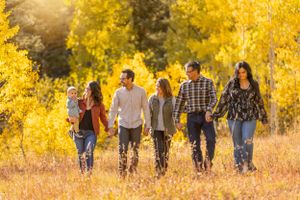 A happy family walks together through a golden autumn field surrounded by yellow aspen trees.