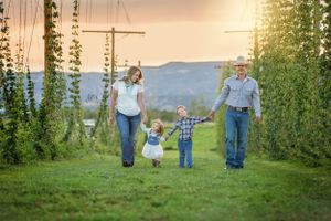 Happy family of four walking through lush green hop field at sunset.