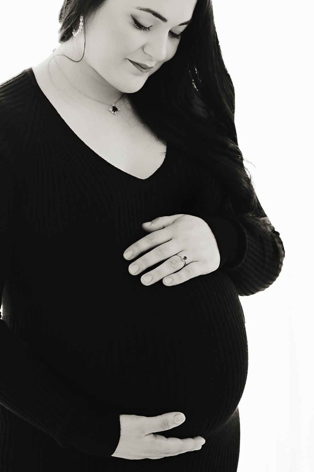 Black and white maternity portraits highlighting gentle hands on pregnant belly.