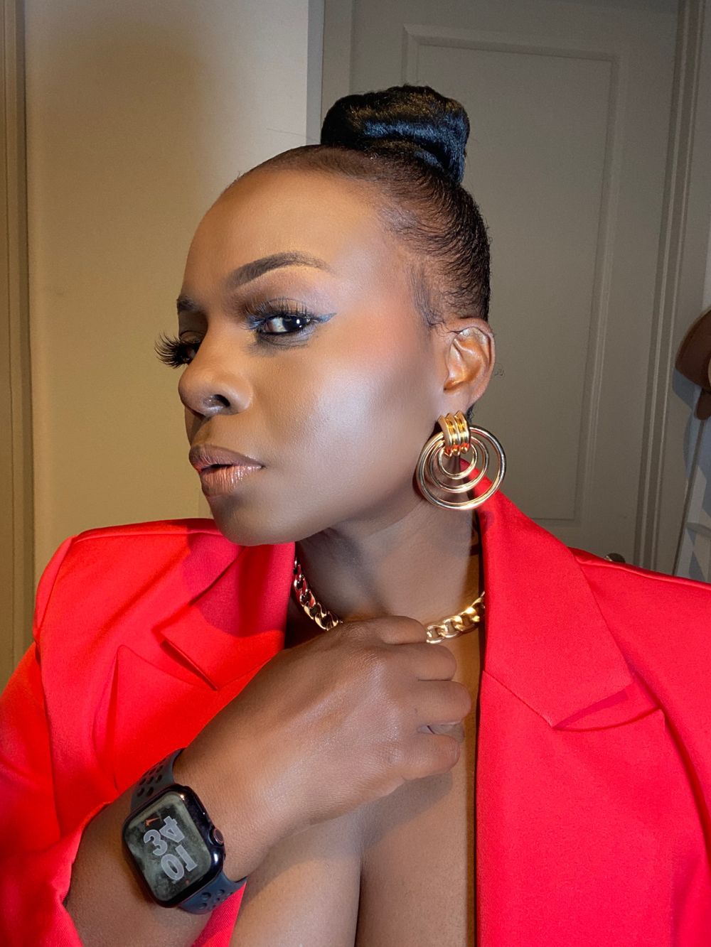 Striking poses in bright red blazer with gold accessories against neutral background.