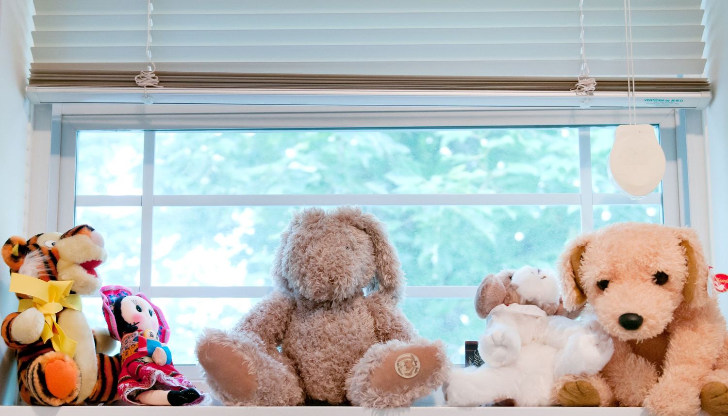 Collection of stuffed animals displayed on a sunny windowsill in a nursery.