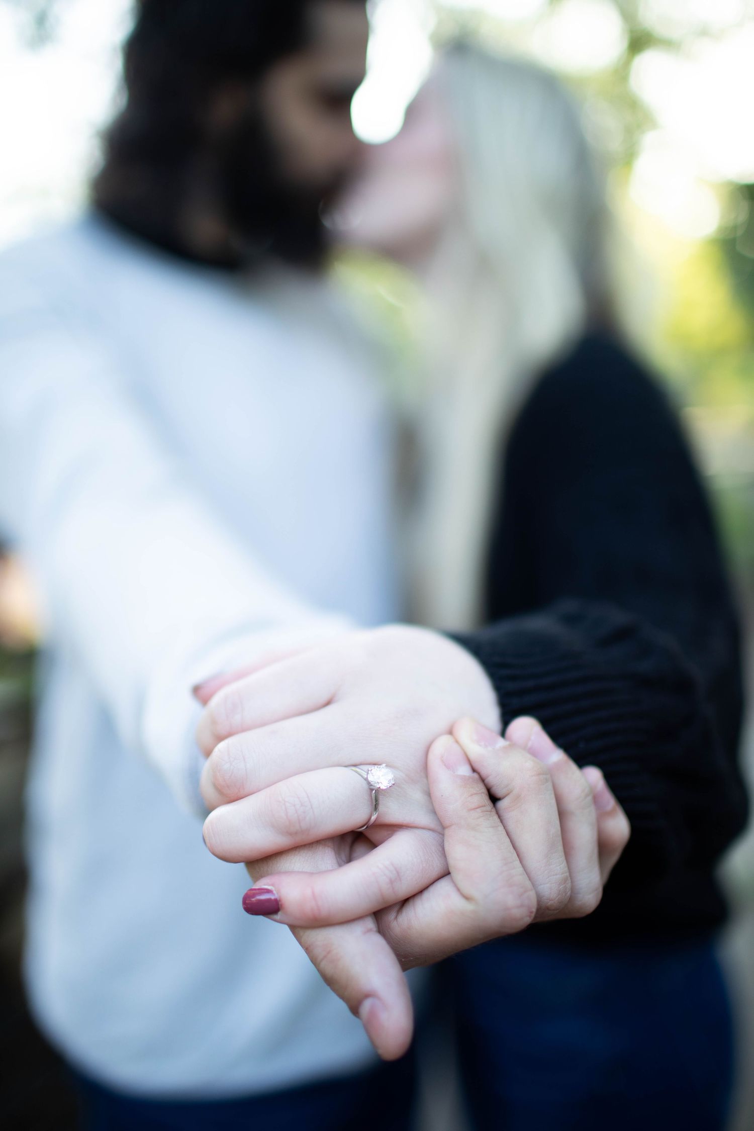 Close-up of couple holding hands showing engagement ring in outdoor setting.