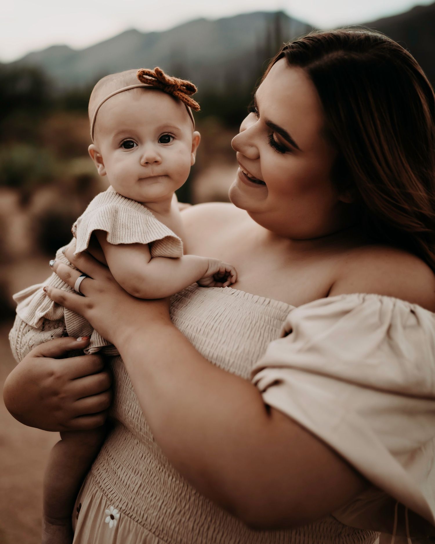 Tender moment between parent and baby against a mountain backdrop at sunset.