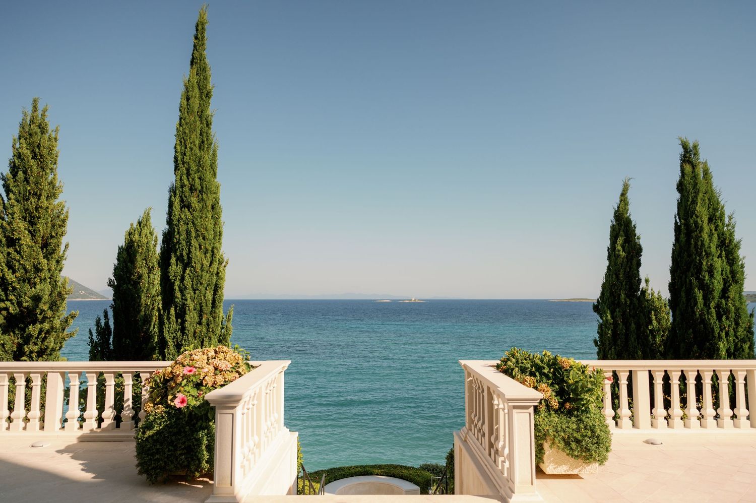 Elegant seaside terrace with cypress trees framing a stunning ocean view.