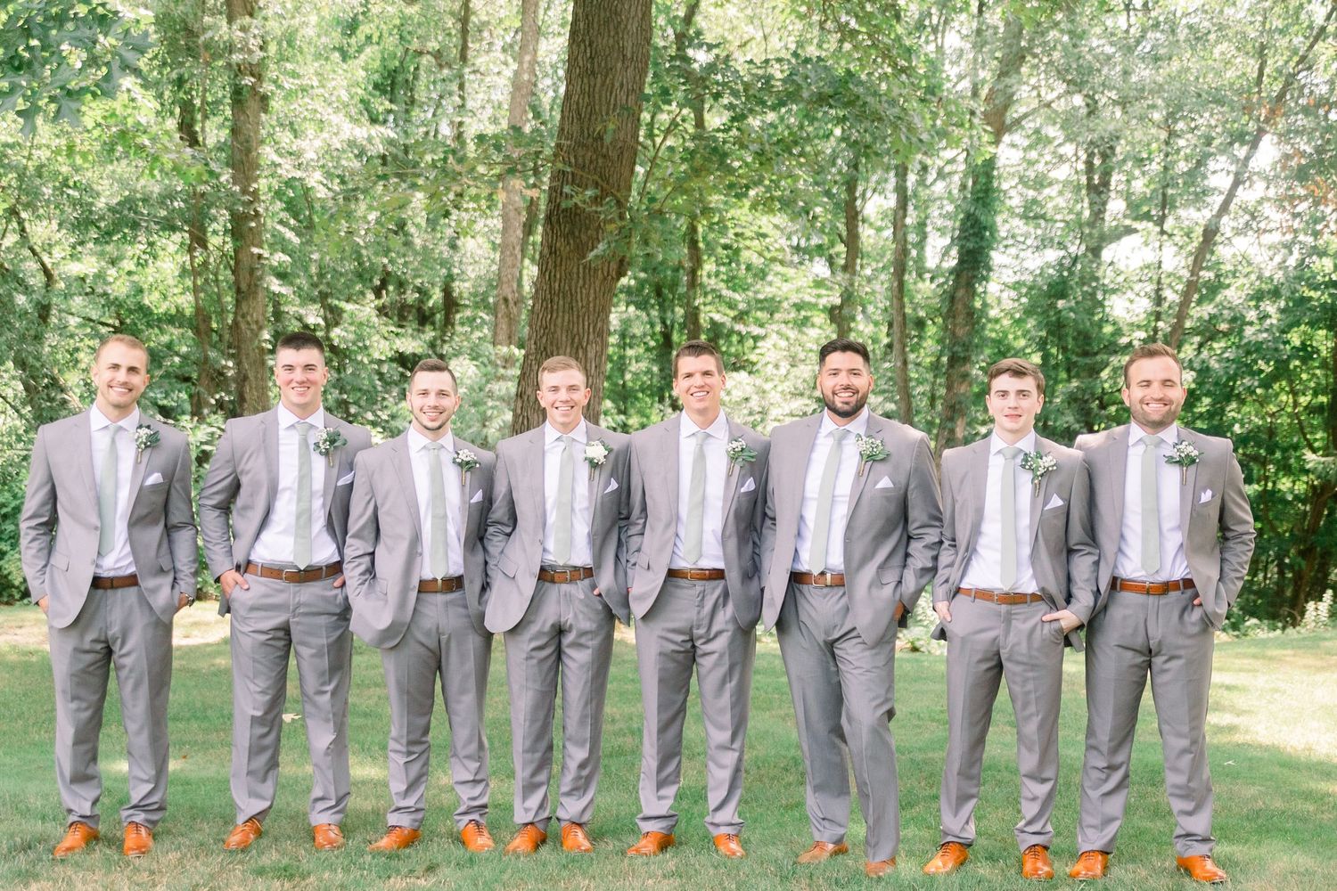 Wedding party in coordinated gray suits and mint ties poses together outdoors in a wooded setting.