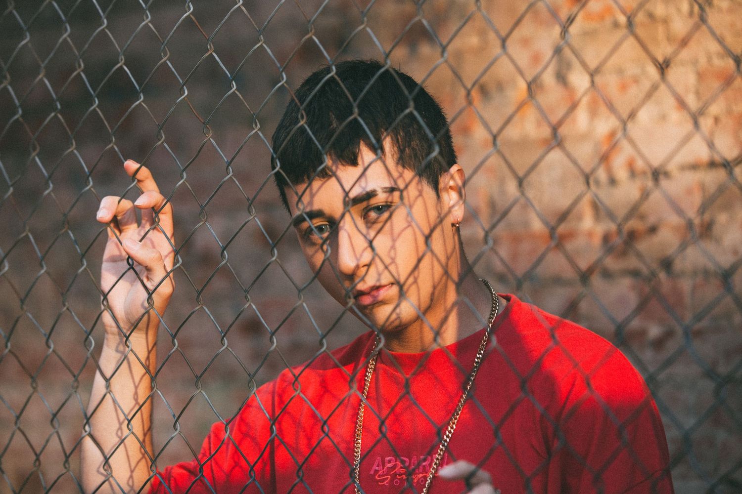 Artistic portrait through chain link fence with red shirt and dramatic lighting.