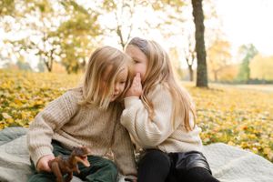 Two figures sharing secrets and giggles while sitting on autumn ground.