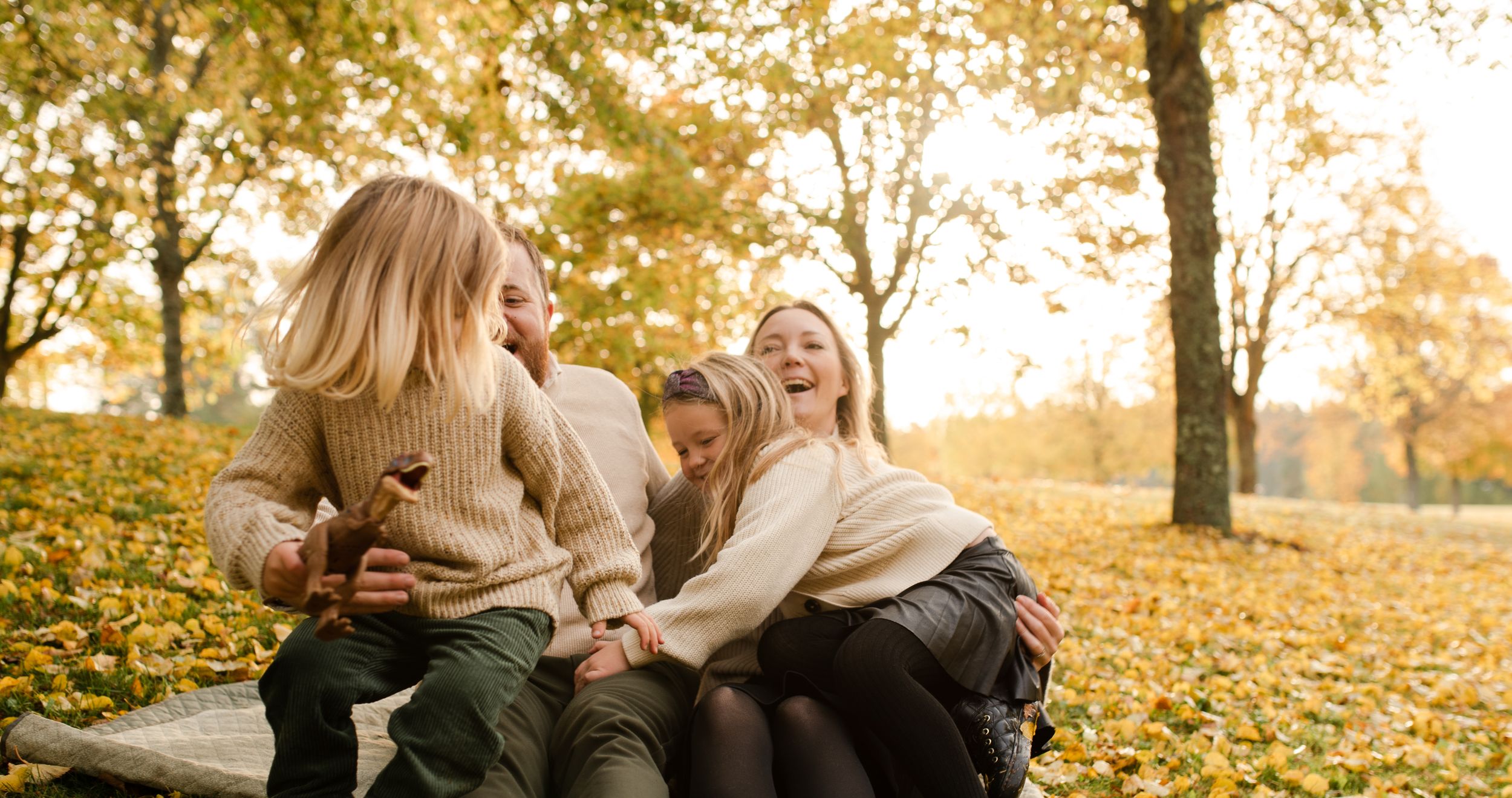 Joyful laughter and bonding moment on fallen autumn leaves in a park.