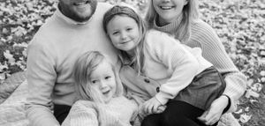 A casual black and white family portrait on fallen leaves outdoors.