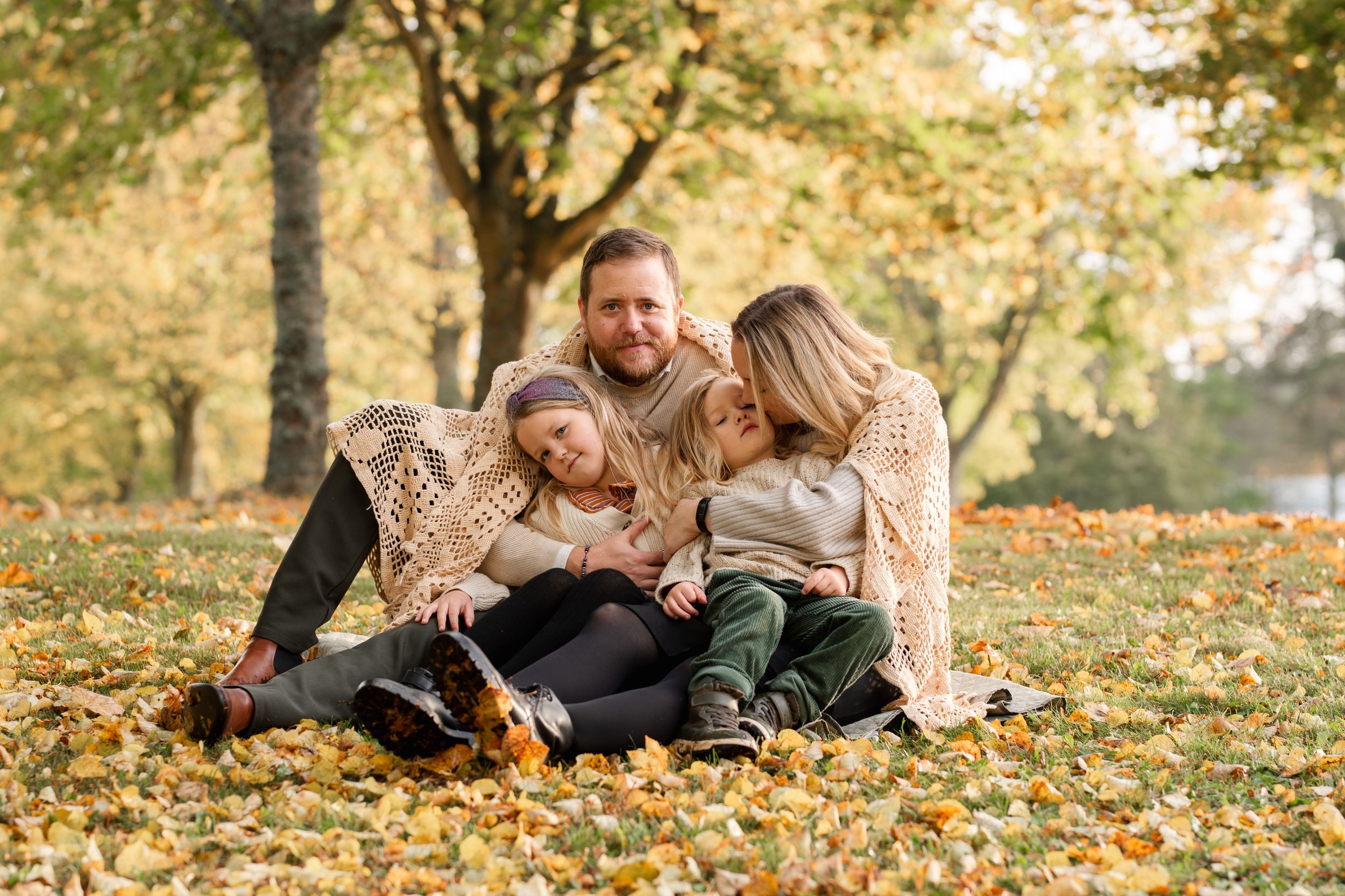 A loving family cuddles together on the ground covered in golden fall foliage.