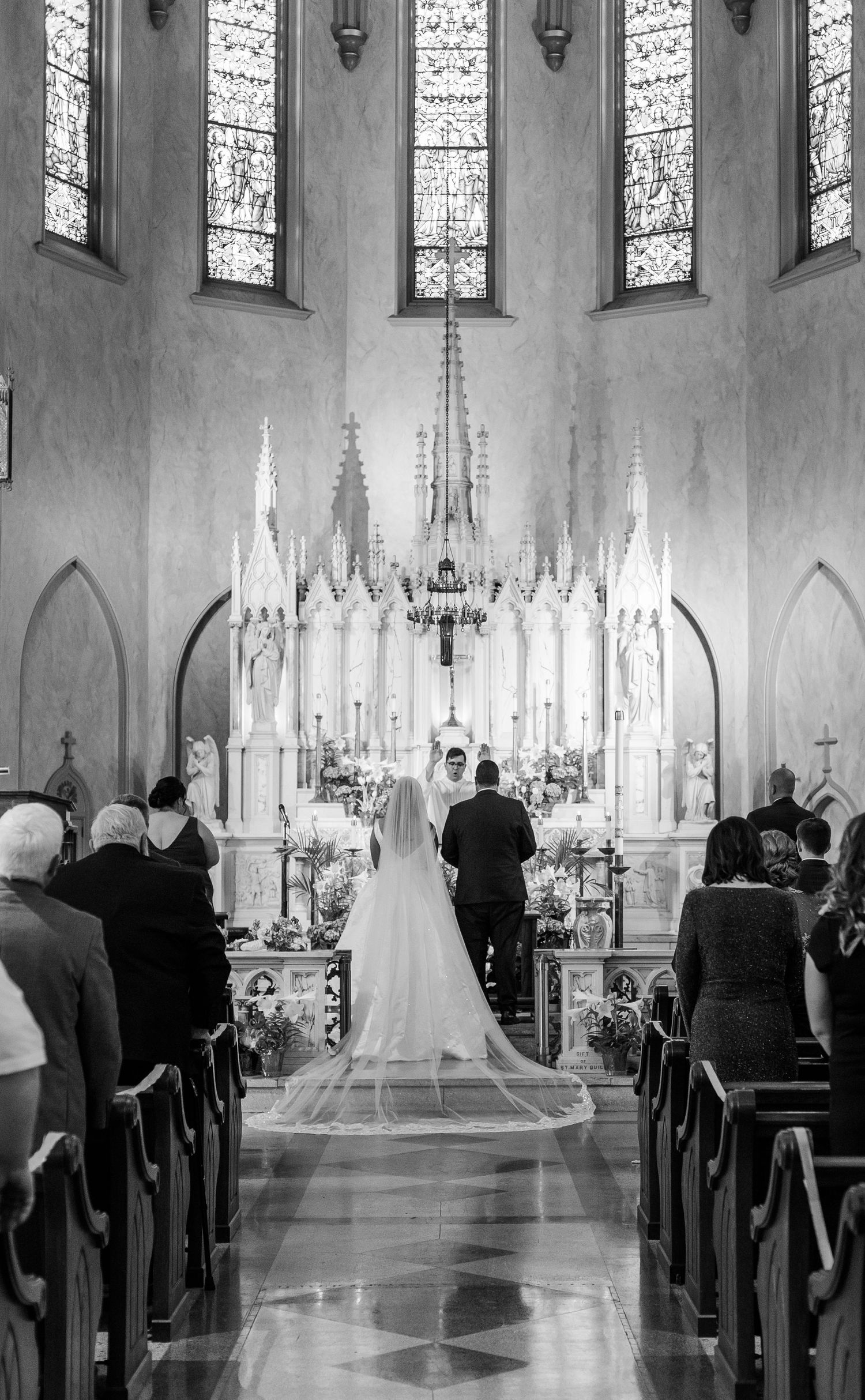 Black and white wedding ceremony photo in Gothic church with dramatic lighting and architecture.