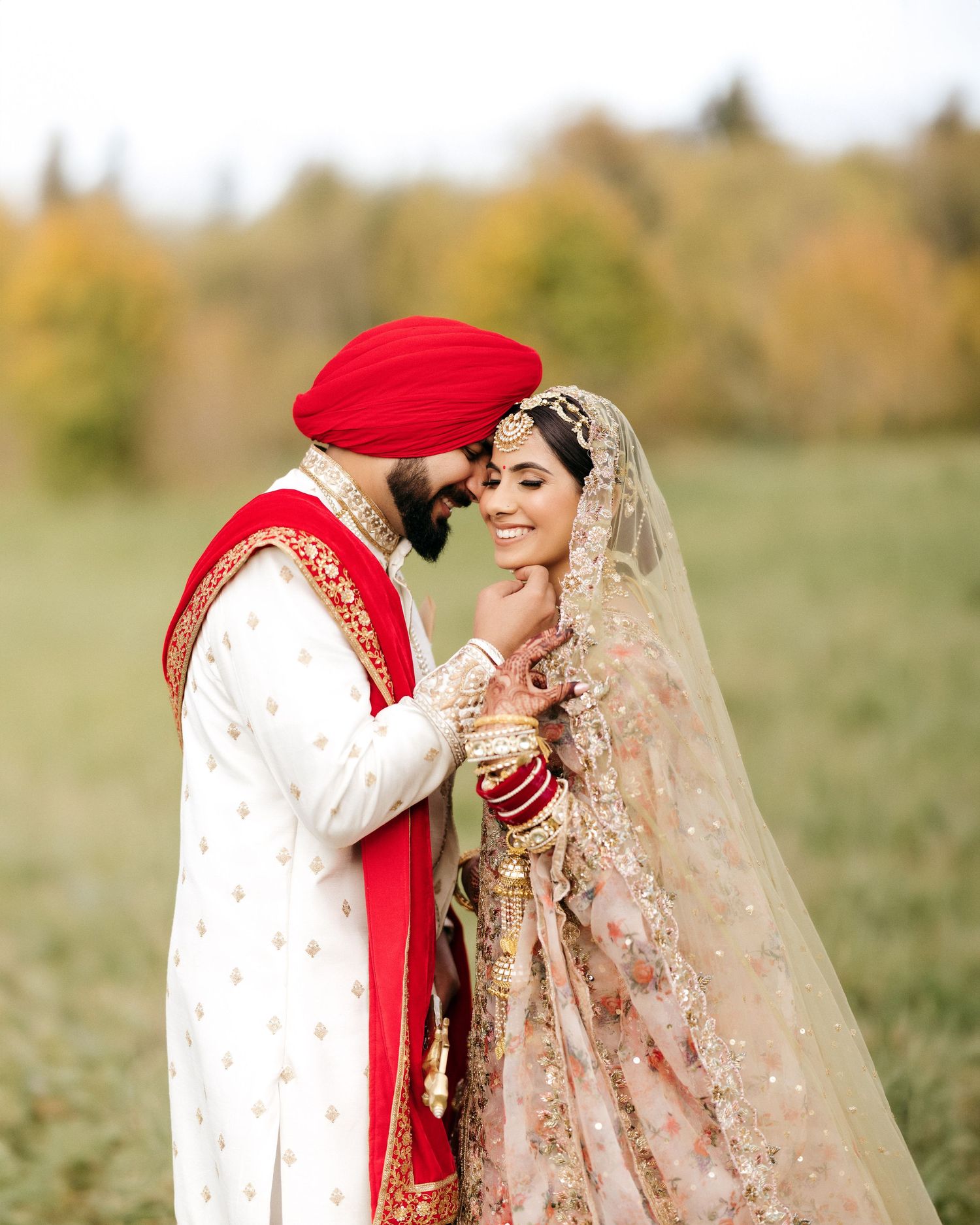 Traditional Indian wedding couple in red and white attire sharing an intimate moment outdoors.