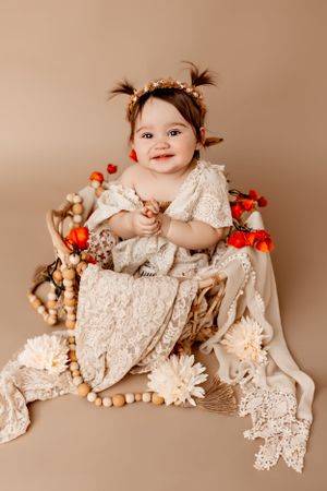 Baby in lace dress surrounded by festive decorations and wooden beads.