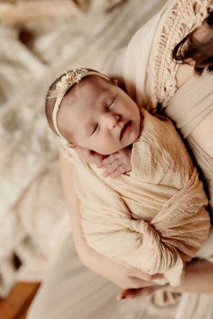 Peaceful sleeping newborn wrapped in soft beige fabric with delicate headband.