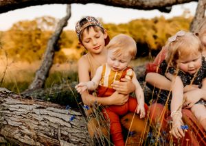 Children sitting on fallen tree trunk in warm autumn sunlight.