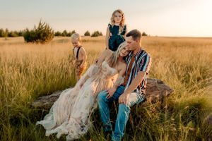 Family enjoying a golden hour photo session while sitting on rocks in a grassy field at sunset.
