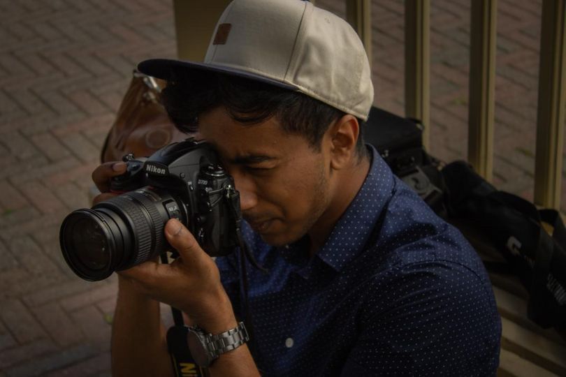 Professional photographer using a DSLR camera with telephoto lens while wearing a baseball cap and polka dot shirt.