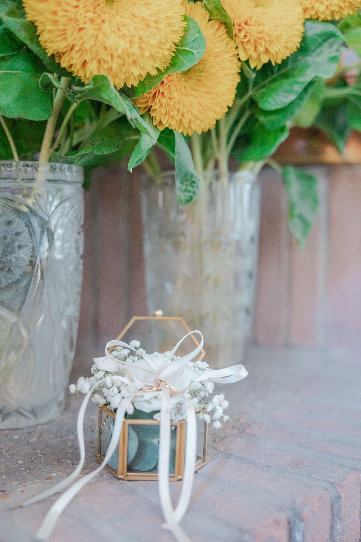 Yellow chrysanthemums in vintage glass vases with delicate white wedding accessories on brick surface.