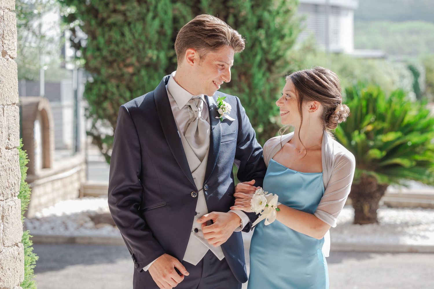 Couple in formal attire share intimate moment on garden path with greenery backdrop.