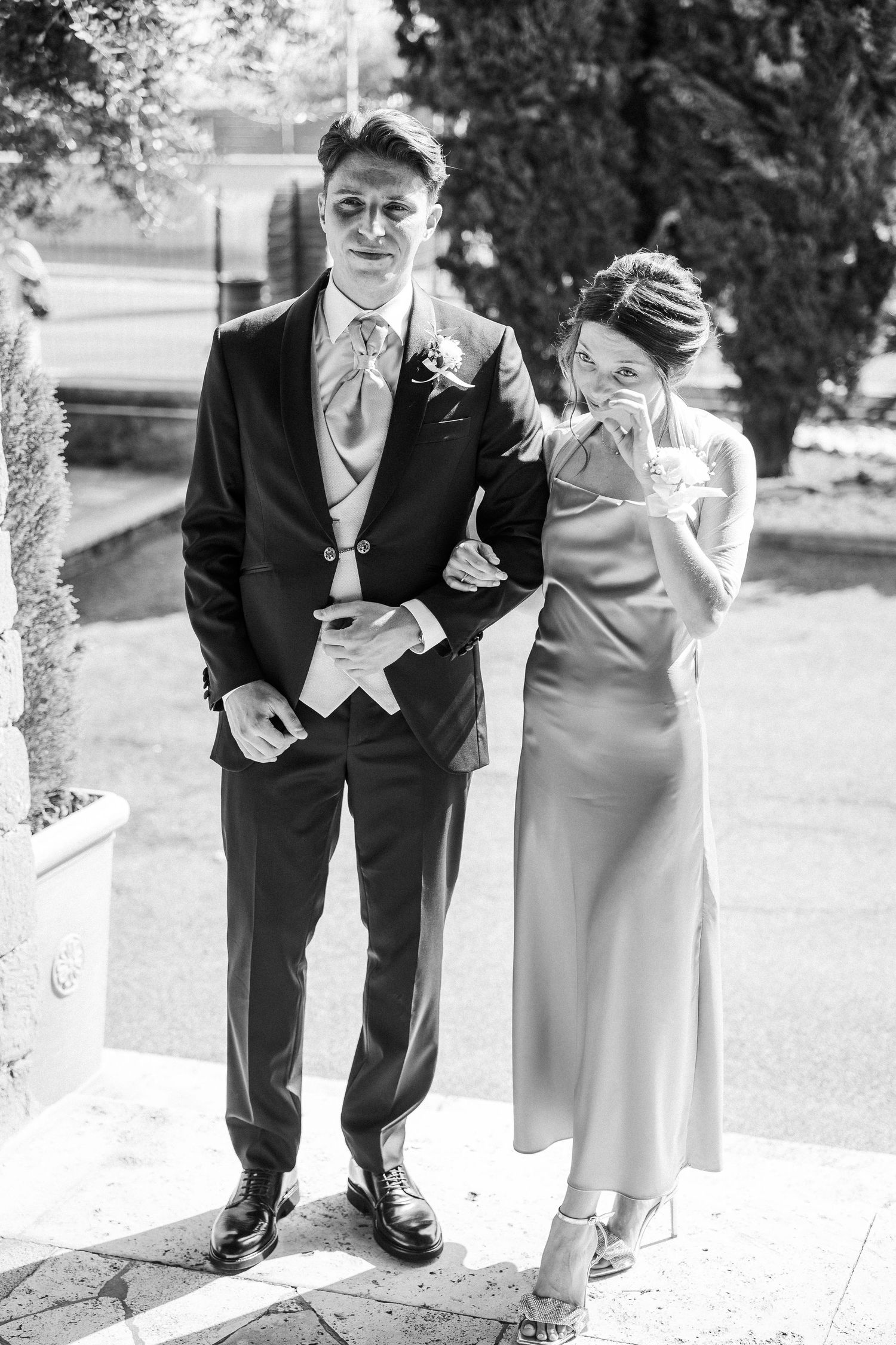 Black and white photo of formal couple sharing a lighthearted moment outdoors.