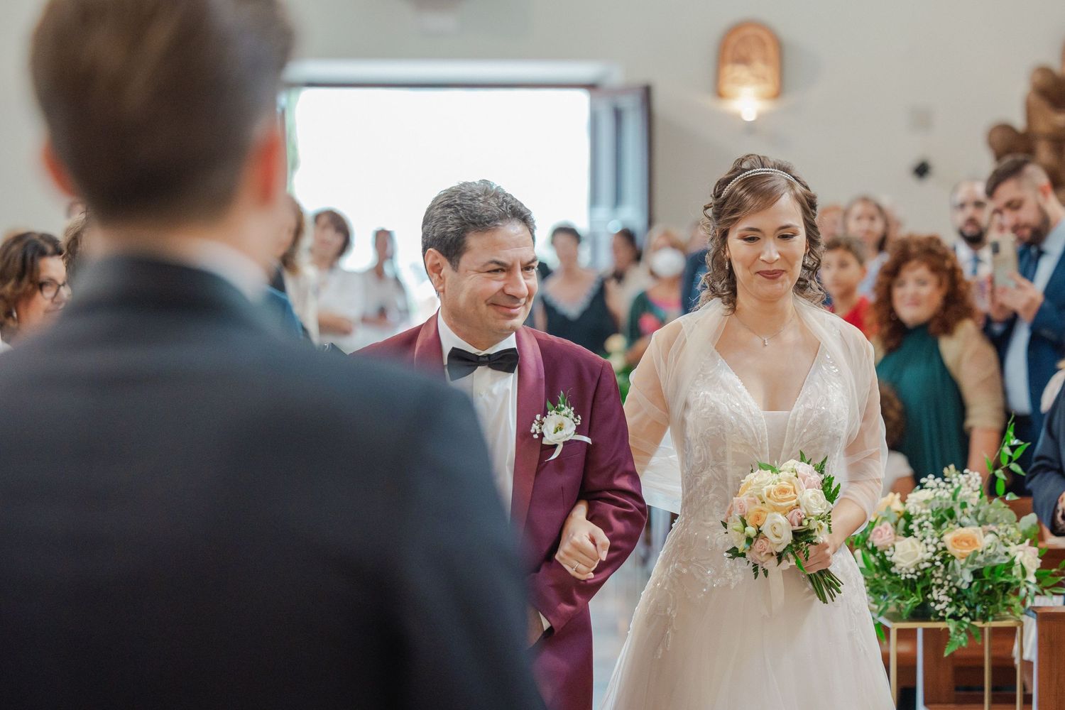 Wedding ceremony processional in church with guests watching from wooden pews.