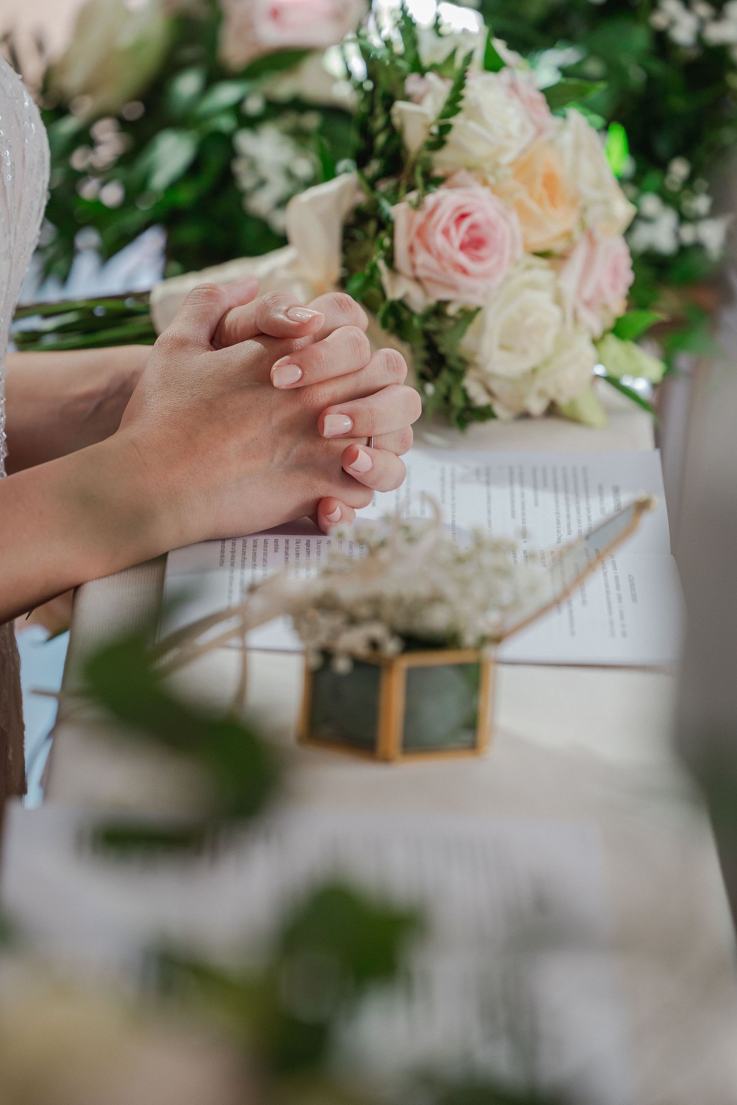 Clasped hands near a bouquet of pink and white roses during a wedding ceremony.
