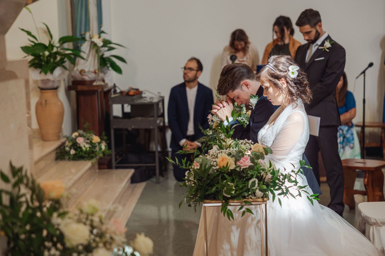 Wedding ceremony in progress inside a decorated church with floral arrangements.