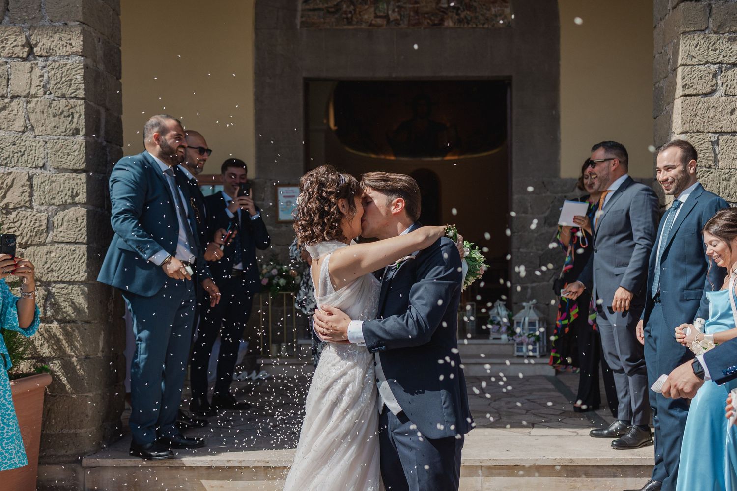 Celebration with confetti shower and guests lined up outside stone church entrance.