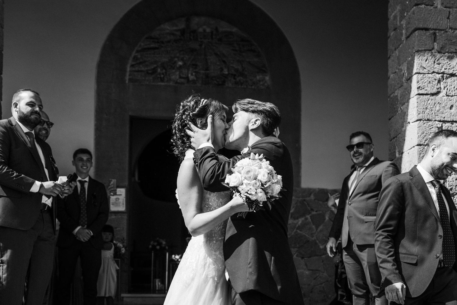 Romantic moment captured in black and white outside church entrance.