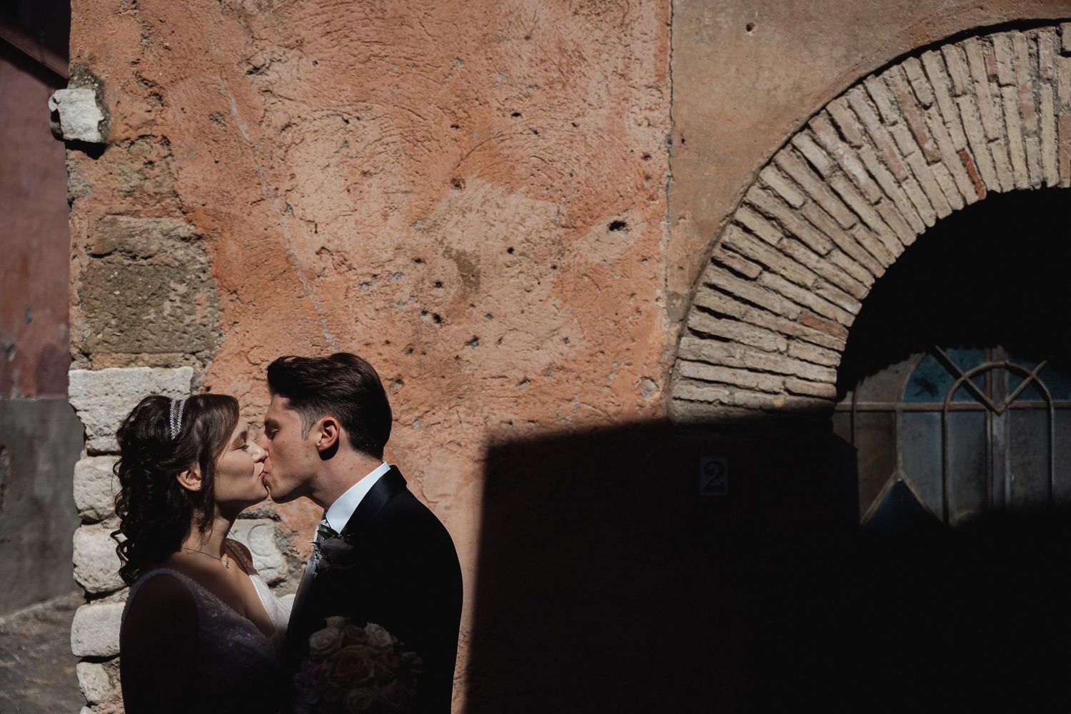 Intimate wedding portrait against a weathered terracotta wall with an arched brick feature.