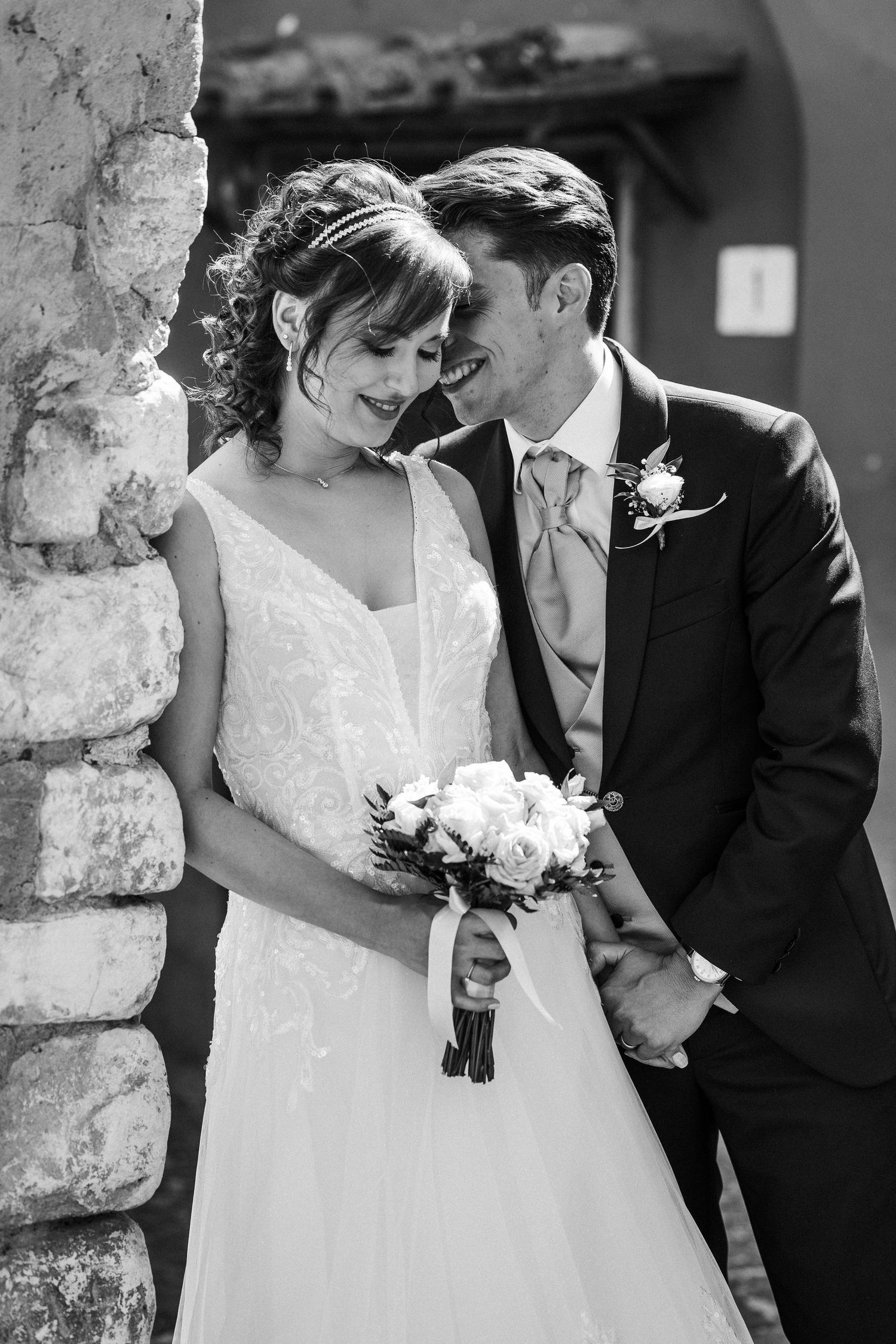 Black and white portrait of newlyweds sharing an intimate moment by a stone wall.