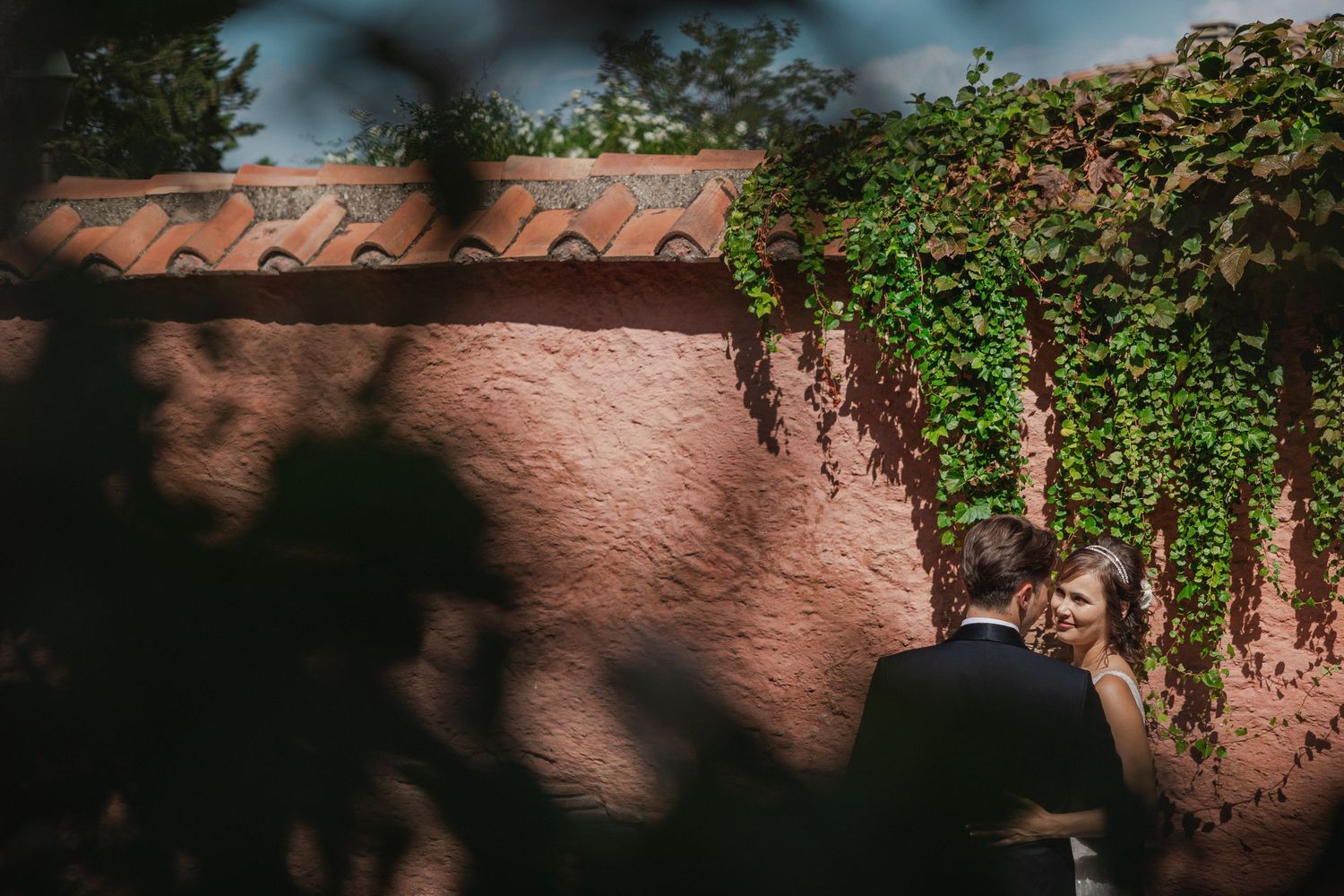 Artistic wedding photo with dramatic shadows and climbing ivy on a terracotta wall.