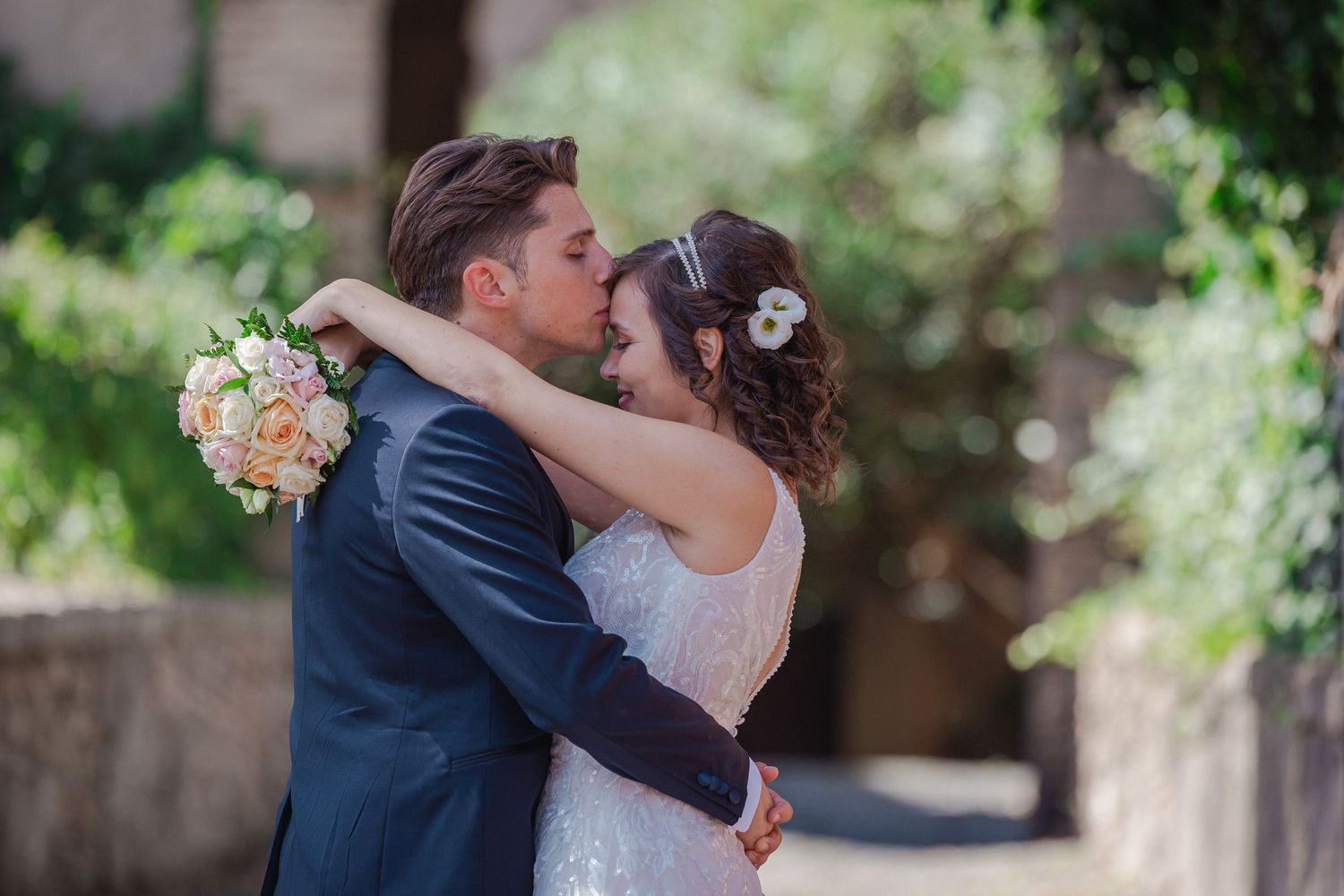Tender embrace between newlyweds with soft peachy bouquet in a garden setting.