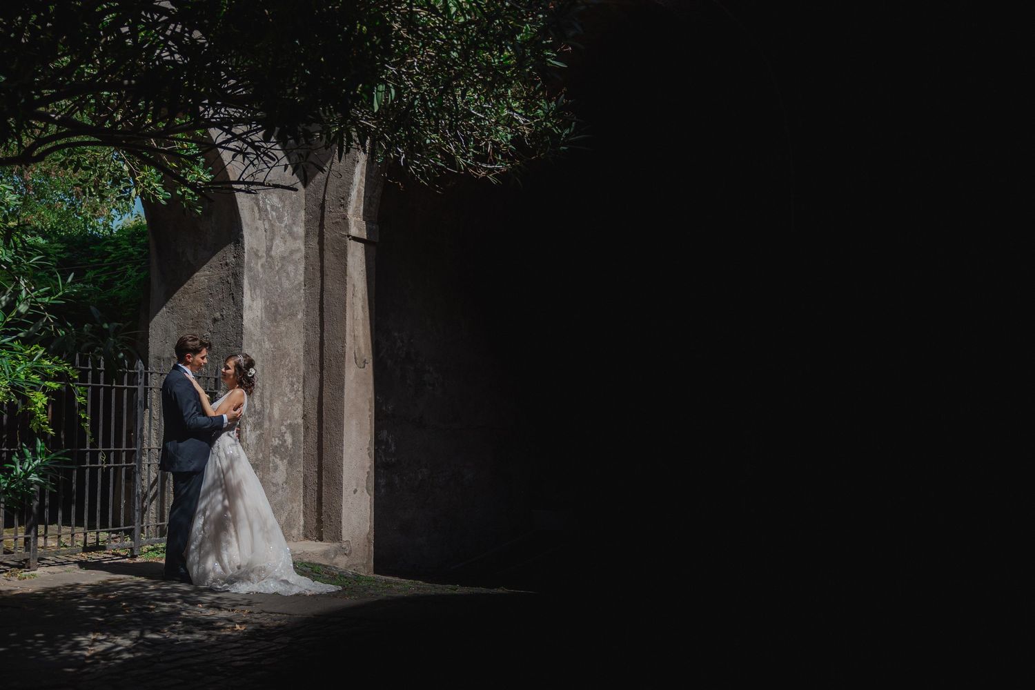 Dramatic wedding portrait framed by stone archway with natural lighting.