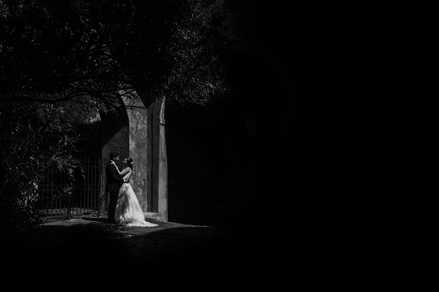 Dramatic black and white wedding portrait highlighted in a dark stone archway.